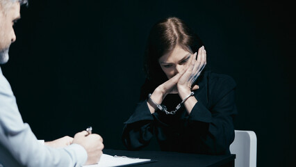Distressed woman in handcuffs sobs in front of the police detective during questioning
