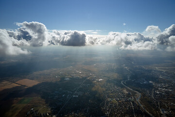 Aerial view from airplane window at high altitude of distant city covered with puffy cumulus clouds...