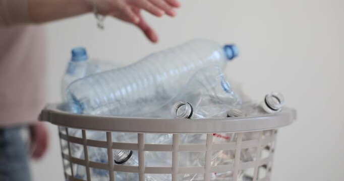 Woman puts empty plastic bottle into bucket for recycling. Female organizes recyclable items to reduce waste and promote sustainability