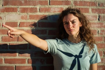 A woman stands in front of a brick wall, pointing with her finger while wearing a suit and tie