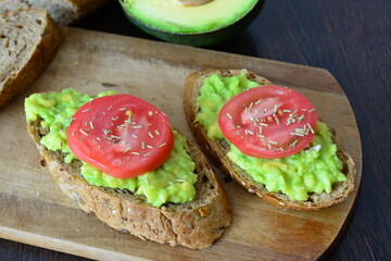 two avocado toasts with tomato slices on a cutting board