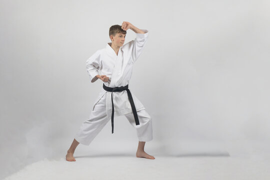 Fifteen year old male teenage karate black belt in long stance doing a head block, studio shot against a white background