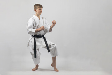 Fifteen year old male teenage karate black belt in a cat stance ready to spar, studio shot against...