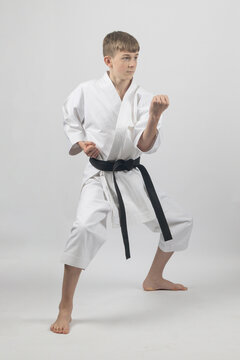 Fifteen year old male teenage karate black belt standing in a low stance doing a body block, studio shot against a white background