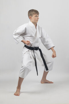 Fifteen year old male teenage karate black belt standing in a low stance doing a low block, studio shot against a white background