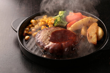鉄板の上で焼く熱々の湯気の上がるジューシーなハンバーグステーキ