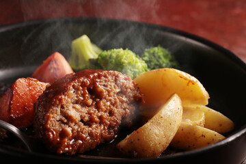 鉄板の上で焼く熱々の湯気の上がるジューシーなハンバーグステーキ