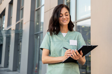 Fototapeta premium Dark-haired young female doctor near the clinic with a prescription list in hands