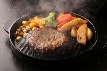 鉄板の上で焼く熱々の湯気の上がるジューシーなハンバーグステーキ