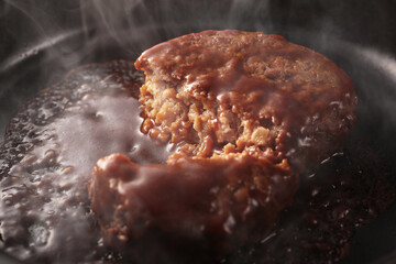 鉄板の上で焼く熱々の湯気の上がるジューシーなハンバーグステーキ