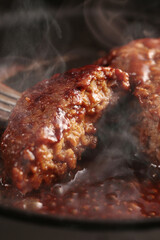鉄板の上で焼く熱々の湯気の上がるジューシーなハンバーグステーキ