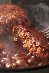 鉄板の上で焼く熱々の湯気の上がるジューシーなハンバーグステーキ