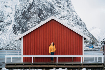 Tourist enjoying winter landscape at red wooden cabin in lofoten islands, norway