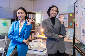 Two businesswomen smiling and making okay sign in office