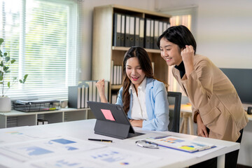 Two businesswomen celebrating success while looking at tablet in office