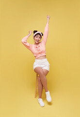 Attractive beautiful Asian teen woman sitting on chair and hands up raised arms success celebration.