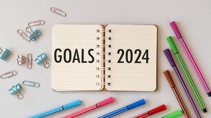 Message Goals 2024 written in notebook, computer keyboard and colorful markers and paper clips white desk, flat lay