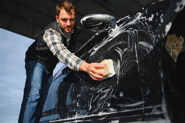A man washes a car with a sponge at a self-service car wash