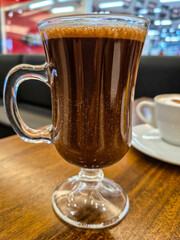 Close up em uma caneca de vidro com chocolate quente, sobre uma mesa de madeira em uma cafeteria no shopping.