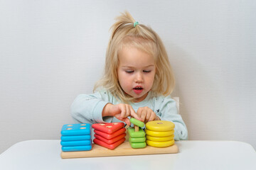 Little child girl toddler is playing collecting a multicolored sorter.