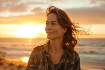 Portrait of a content caucasian woman in her 40s dressed in a relaxed flannel shirt while standing against beautiful beach sunset
