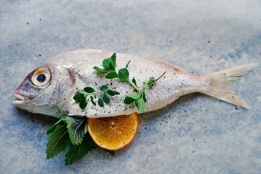Overhead view of a whole Sea bream stuffed with with orange and fresh herbs on a table