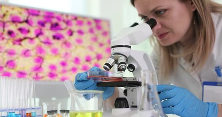 Woman researcher puts Petri dish with biomaterial sample on microscope. Female assistant works with materials testing specimens in lab