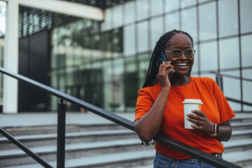 Smiling Woman Talking on Smartphone While Holding Coffee Cup Outdoors