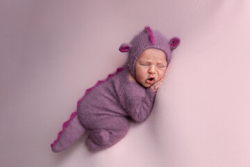 Little adorable newborn baby girl sleeping in a hat with dragon ears. Neutral background. Studio shot of a ten-day-old newborn baby. Beginning of life. Fairy tale. Dragon toy