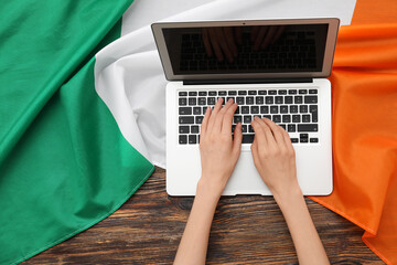 Female hands with modern laptop and flag of Ireland on wooden background