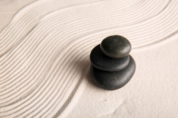 Stack of black stones on light sand with lines. Zen concept