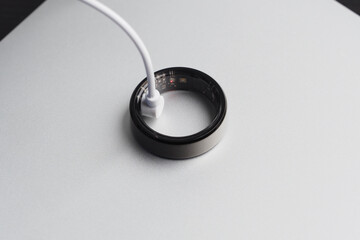 Smart ring is connected to a charging cable resting on a minimalist surface, illustrating...