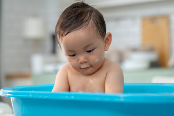 Asian baby taking a bath in a blue tub at home.