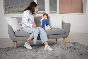 Angry mother threatening her little daughter on sofa at home. Domestic violence concept