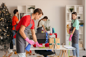 Obraz premium Male janitor cleaning table and his team in office after New Year party