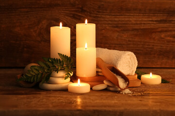 Spa composition with burning candles, stones and fern leaves on dark wooden background