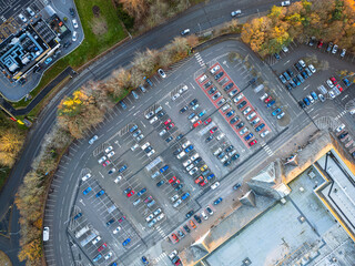 Drone top down view of a large customer car park seen at a well known, British supermarket store. Park of a town's ring road can be seen around the car park.