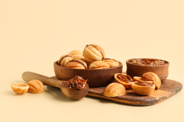 Wooden board and bowl of sweet walnut shaped cookies with boiled condensed milk on yellow background