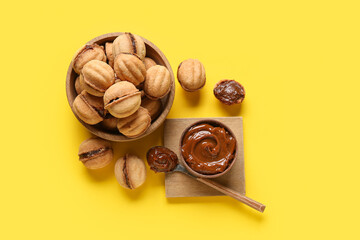 Wooden bowl with sweet walnut shaped cookies with boiled condensed milk on yellow background
