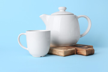 White ceramic empty mug and tea pot on board on blue background