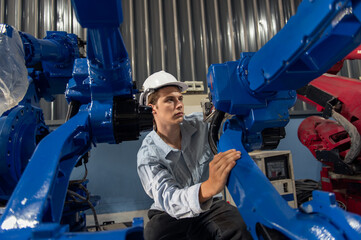 Engineer standing by robotic arm and operating machine in industry factory, technician worker check for repair maintenance electronic operation