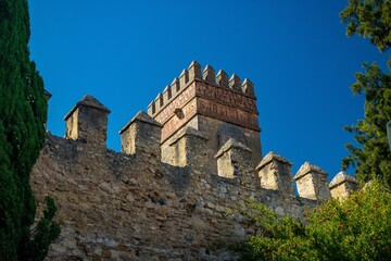 Historic stone fortress wall with battlements against a clear blue sky in Spain