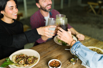 Friends joyfully raise their glasses while savoring tacos and refried beans at a lively mexican taqueria