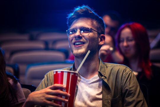Guy watches a movie in the cinema and drinks juice.