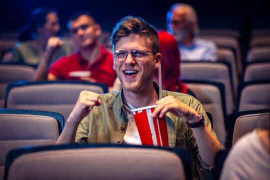 Guy watches a movie in the cinema and drinks juice.