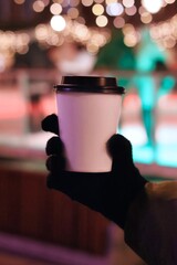 Mockup of a mug in a gloved hand against the background of Christmas lights