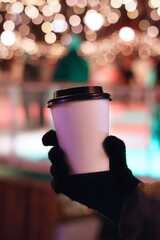 Mockup of a mug in a gloved hand against the background of Christmas lights