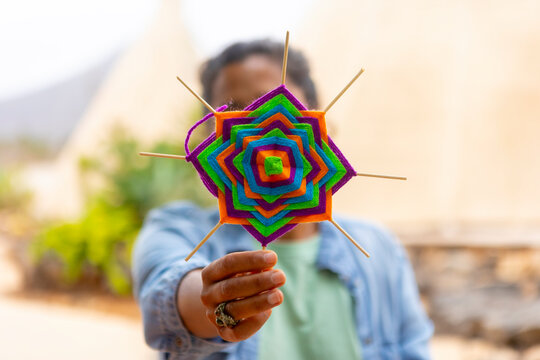 Colorful handcrafted Ojo de Dios held by person outside
