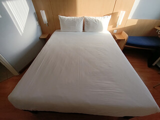 A bed with white sheets and pillows in a hotel room