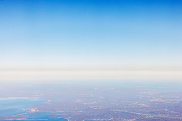Aerial view of coastline and sprawling land from airplane window during clear sunny day with...